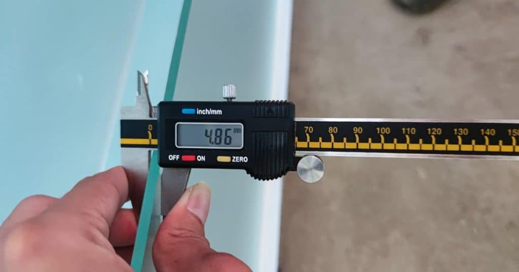 A close-up of someone using a black digital caliper on a glass panel. The digital caliper reads 4.86.