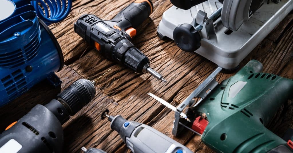 Various power tools lying on a wooden table. The tools include a drill, grinder, and other related items.