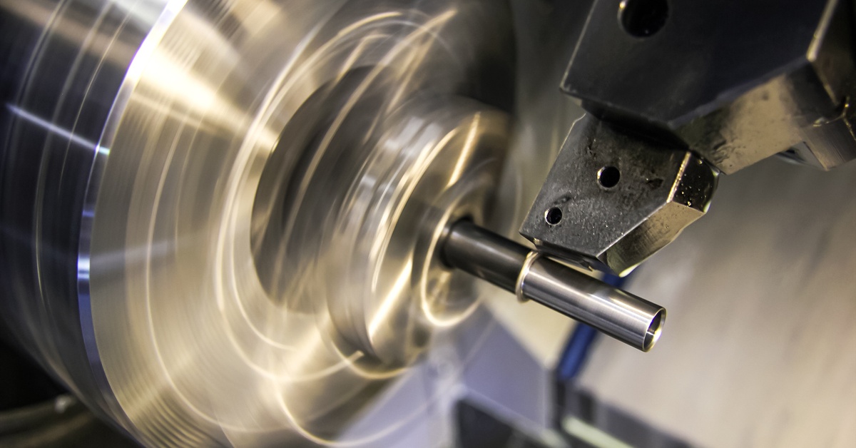 A close-up of a carbide tool sharpening a metal component. The component has a square-like shape with a slope.