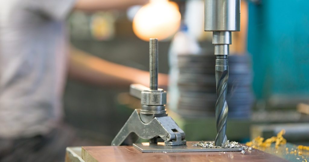 A close-up of a high-speed steel drill bit cutting through material. Another long drill bit sits beside it.