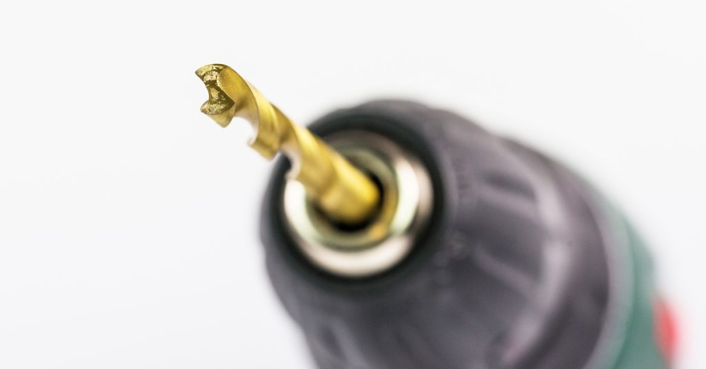 A close-up and slightly blurred power drill with a titanium-coated drill bit. The drill is black, green, and red.