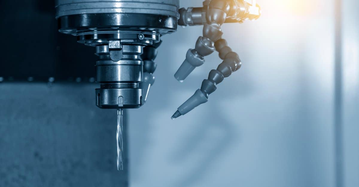 A close-up of a bright light reflecting off of a small gray machine reamer tool on a metal CNC machine.