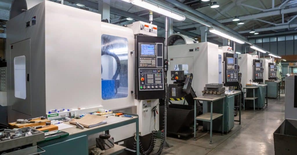 A row of CNC machines in a factory with a green workstation holding tools and supplies near each one.