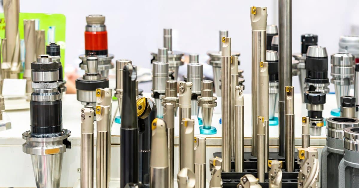 A table with dozens of end mills, drill bits, and other cutting tool parts displayed upright against a white background.