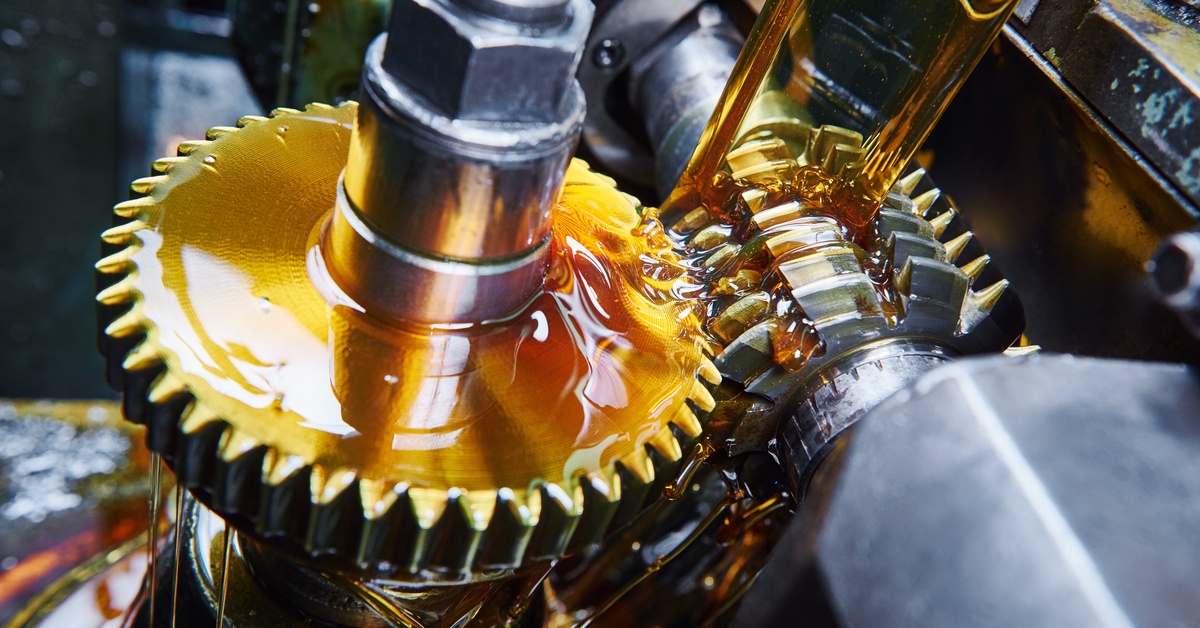 A close-up of lubricant falling onto machine gears. The lubricant has a thick consistency with an amber color.